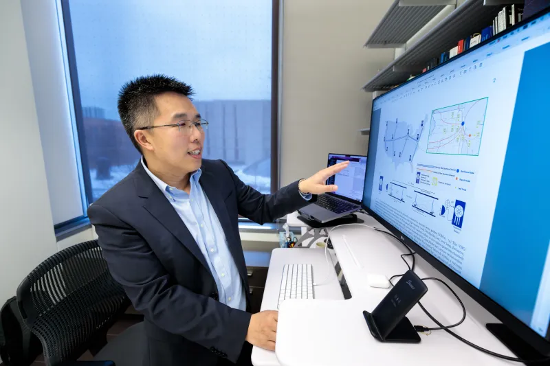 Faculty Liang Jiang pointing towards computer